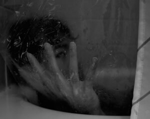 A black and white photo of a man sitting in a bathtub with his hand in front of his face in focus
