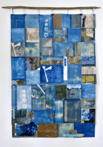 Tapestry hanging from stick organized in square pieces of different shades of blue and white