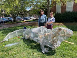 Nyssa and Carson stand behind the skeleton of their marine iguana sculpture in front of Morehead Planetarium