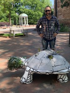 Artist Nico Amortegui stands behind his tortoise sculpture with The Well in the background