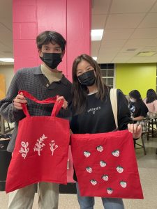 Students hold up red tote bags with painted plants and strawberries